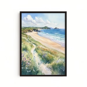 May include: Watercolor painting of a coastal landscape with a sandy beach, blue ocean, and green cliffs under a bright sky. A path winds through tall grass and wildflowers in the foreground. The artwork is framed in a dark brown wooden frame.