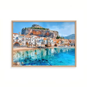 May include: A framed watercolor print of a coastal town with white buildings, orange roofs, and a large cliff. The clear turquoise water reflects the buildings and the blue sky. The artwork is in a light wood frame.