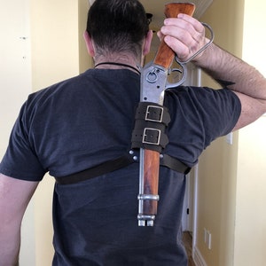 May include: A person wearing a dark blue shirt with a leather shoulder holster and a silver and wood rifle.
