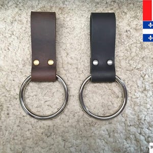 May include: Two leather belt loops with metal rings. One loop is brown leather and the other is black leather.