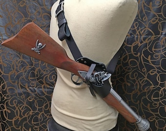 May include: A black leather shoulder holster with a silver buckle and a wooden pistol with a silver skull and crossbones design. The pistol is held in the holster and has a silver barrel.