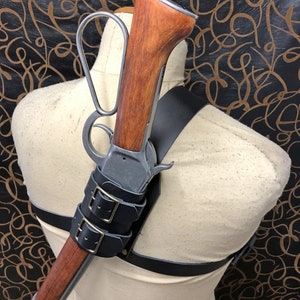 May include: A leather shoulder holster with a rifle attached. The rifle has a wooden stock and a metal barrel. The holster has two buckles and is made of black leather.