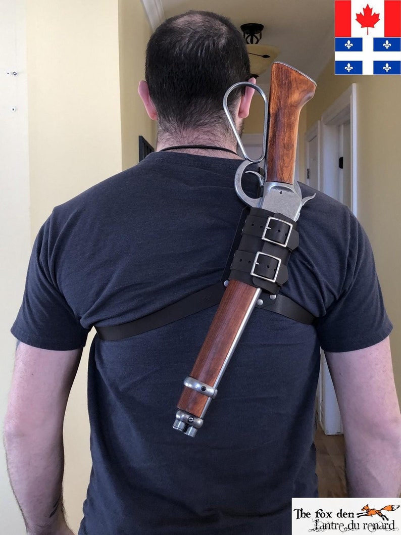 May include: A person wearing a dark blue t-shirt is carrying a rifle on their shoulder using a leather shoulder strap. The rifle has a wooden stock and a metal barrel.