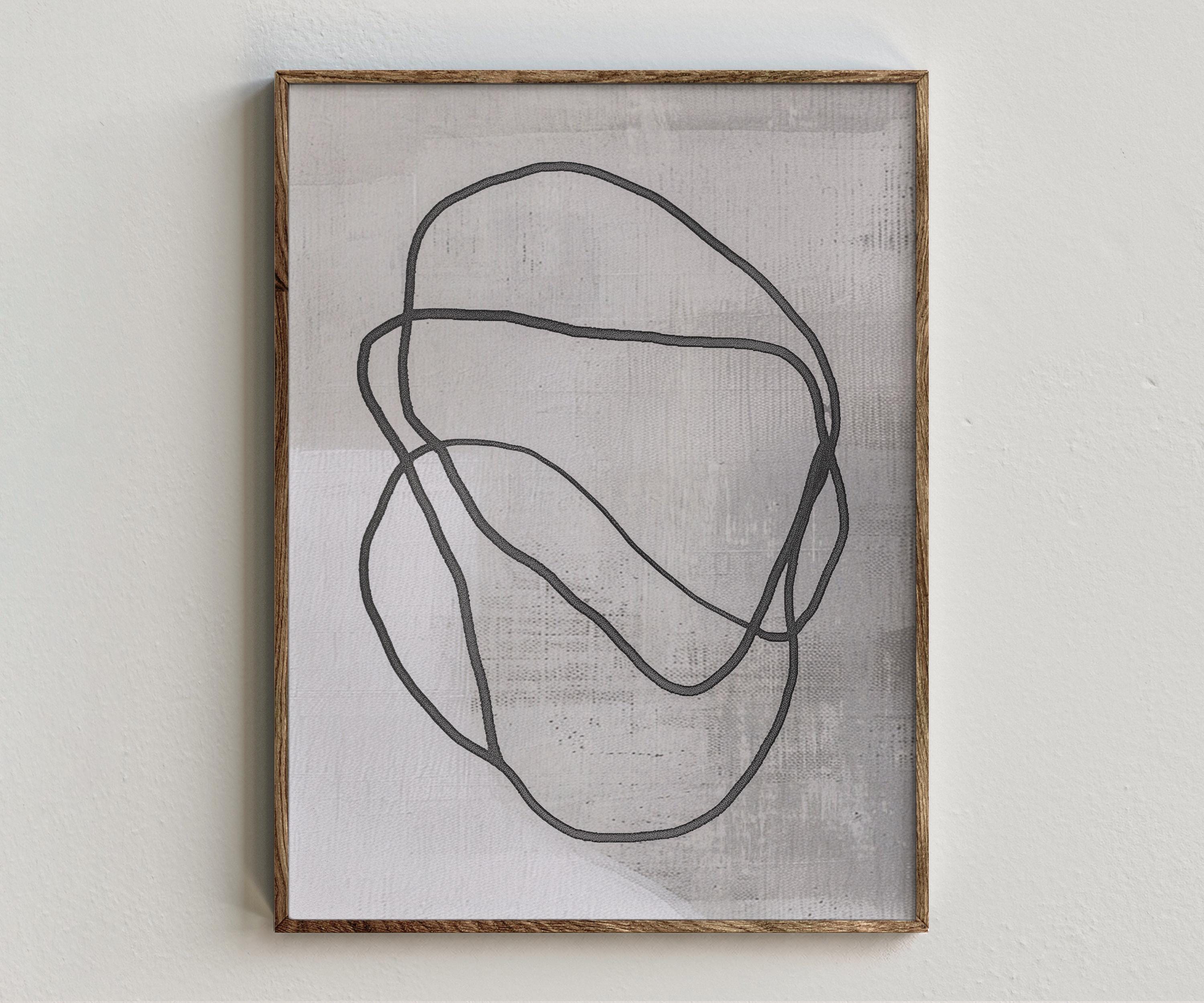 Framed artwork “Atomico” showing abstract face composition with black linework, a soft grey ground, and minimal modern portrait style on a white wall.