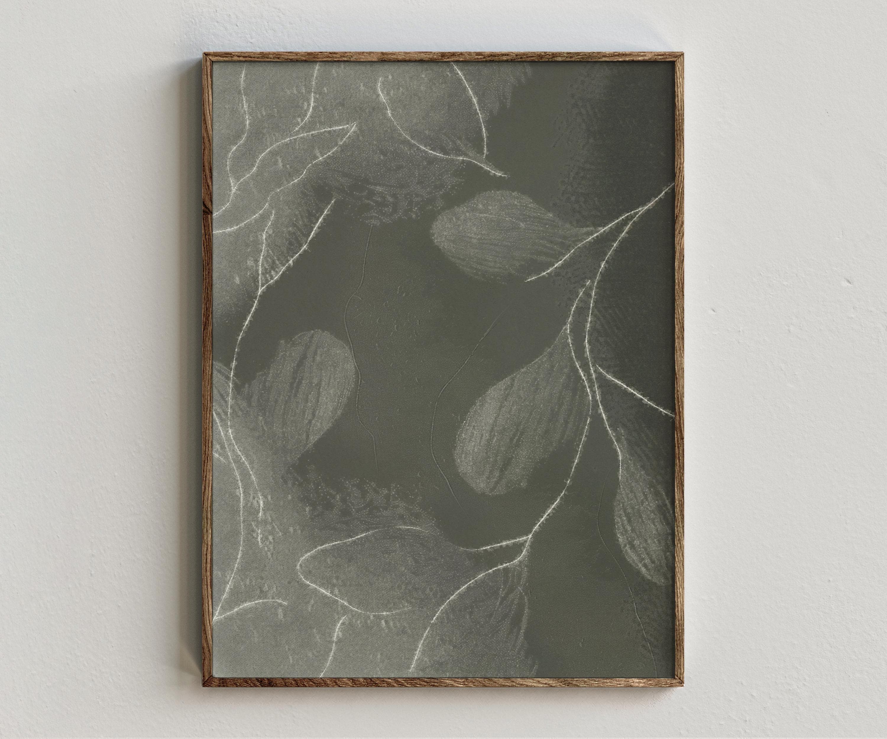 Framed artwork “Susurrance” showing dark botanical composition with muted green leaves, pale branch lines, and soft textured nature style on a white wall.