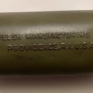 May include: An olive-green, cylindrical metal object with rounded ends. The text "WELSH MANUFACTURING CO. PROVIDENCE, R.I. U.S.A." is embossed on the side. The object has a slightly worn appearance.