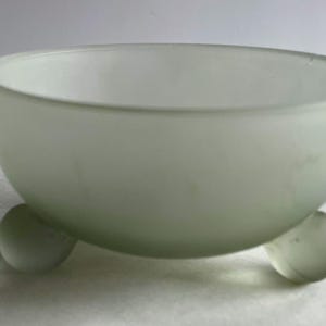 May include: A frosted glass bowl with a rounded shape, resting on three small, spherical feet. The bowl has a soft, translucent appearance, and the overall design is simple and elegant. The bowl is suitable for serving or display.