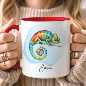 May include: White ceramic mug with a red interior and handle. The mug features a colorful watercolor illustration of a chameleon on a branch, set against a blue background. The name "Evan" is written in script below the image.