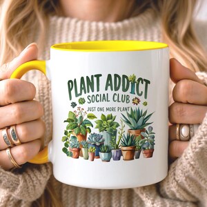 May include: A white ceramic mug with a bright yellow handle and interior rim. The front features a colorful illustration of various potted succulents and cacti with the text "PLANT ADDICT SOCIAL CLUB" and "JUST ONE MORE PLANT" in green.