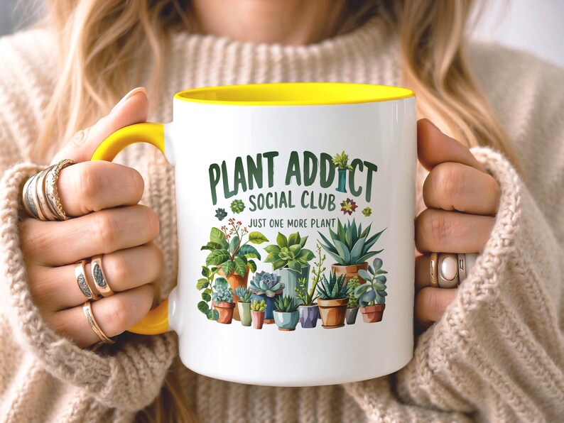 May include: A white ceramic mug with a bright yellow handle and interior rim. The front features a colorful illustration of various potted succulents and cacti with the text "PLANT ADDICT SOCIAL CLUB" and "JUST ONE MORE PLANT" in green.