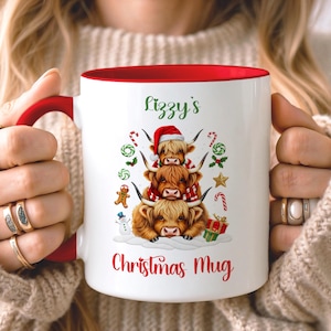 Può includere: Tazza in ceramica bianca con interno e manico rossi, con un design festivo. La tazza mostra tre mucche delle Highlands impilate, con cappelli e sciarpe di Babbo Natale, con la scritta "Lizzy's Christmas Mug".