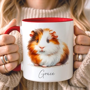 May include: White ceramic mug with a red interior and handle, featuring a watercolor illustration of a guinea pig in shades of brown, orange, and white. The name "Grace" is written in script below the guinea pig.