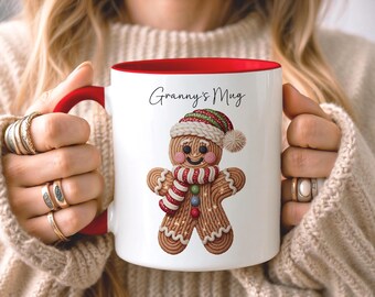 May include: A white ceramic mug with a red interior and handle, featuring a graphic of a gingerbread person wearing a red, green, and white knit hat and scarf. The text "Granny's Mug" is printed in black script above the gingerbread character.