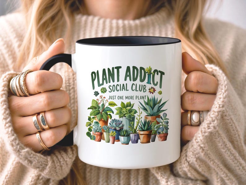 May include: A white ceramic mug with a black handle and rim, featuring a colorful graphic of various potted succulents and plants. The text reads "PLANT ADDICT SOCIAL CLUB" in green letters above the phrase "JUST ONE MORE PLANT" in smaller black text.