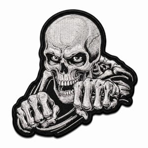 Könnte beinhalten: Ein gestickter Aufnäher mit einem detaillierten weißen Totenkopf mit bedrohlichem Ausdruck, abgebildet ab der Brust. Die Skelettfigur hält ihre knöchernen Hände nach vorne, als würde sie ein Lenkrad greifen, umrandet von einem dicken schwarzen Rand.
