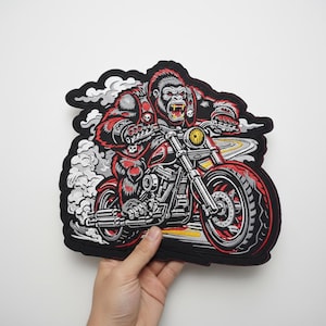 Puede incluir: Parche bordado con un gorila montando una motocicleta. El gorila es rojo y gris, con una expresión feroz y un chaleco con detalles de calaveras. La motocicleta es roja y plateada, con humo y un diseño de carretera en el fondo.
