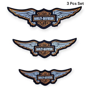 May include: Three Harley-Davidson patches with a winged design. Each patch features the Harley-Davidson logo in a rectangular frame, with the words "MOTOR HARLEY-DAVIDSON CYCLES". The wings are light blue with gold and black trim. The text "3 Pcs Set" is at the top.