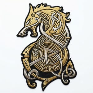 May include: An embroidered patch featuring a stylised wolf head in profile with intricate gold and silver metallic thread detailing. The design incorporates complex Celtic knotwork and geometric patterns against a solid black background.