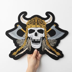 May include: Embroidered patch featuring a skull wearing a Viking helmet with crossed axes. The skull is white with a detailed design, and the helmet is gold with horns. The axes are gray and gold, set against a black background.