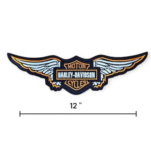 May include: A black, embroidered Harley-Davidson patch in a wing design, measuring 12 inches across. The patch features the Harley-Davidson logo in a rectangular frame, with the words "MOTOR CYCLES". The wings are outlined in gold and light blue.