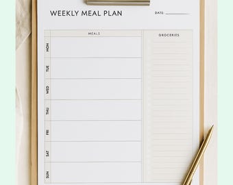 May include: A wooden clipboard holds a white paper with a "WEEKLY MEAL PLAN" title. The plan includes sections for meals and groceries, with a gold pen resting on the paper. The clipboard is secured with a silver metal clip.