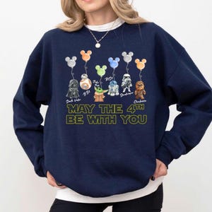 May include: Navy blue sweatshirt with Star Wars characters as balloons, including Darth Vader, BB-8, and Chewbacca. The text "MAY THE 4TH BE WITH YOU" is printed in yellow. The balloons have Mickey Mouse ears.