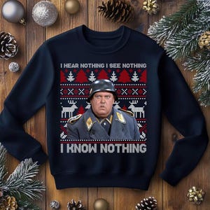 May include: Navy blue Christmas sweater with a festive pattern and the phrase "I HEAR NOTHING I SEE NOTHING I KNOW NOTHING." The sweater features a portrait of a man in a military uniform and helmet. The design includes red, white, and black elements.