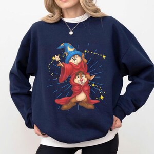 May include: Navy blue sweatshirt featuring a cartoon illustration of two chipmunks dressed as wizards. One chipmunk wears a blue wizard hat and red robe, holding a wand. The other chipmunk is in a red robe. Yellow stars and blue lines radiate from the chipmunks.