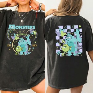 May include: Dark gray t-shirt featuring a Monsters University design. The front graphic includes the text "Monsters University EST 2013" with Sully and Mike Wazowski. The back features the same characters on a checkered background.