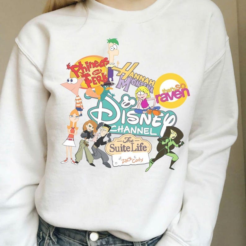 Pode incluir: Camisola branca com gr&aacute;ficos coloridos de desenhos animados de programas do Disney Channel, incluindo "Phineas e Ferb", "Hannah Montana", "As Vis&otilde;es da Raven" e "Zack & Cody: G&ecirc;meos em A&ccedil;&atilde;o". O design &eacute; uma colagem de personagens e logotipos.