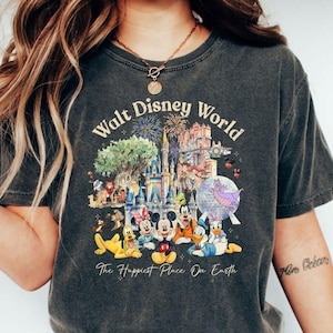 May include: Dark gray t-shirt featuring a colorful graphic of Walt Disney World characters and landmarks. The design includes Mickey Mouse, Minnie Mouse, Donald Duck, and other beloved characters, with the text "Walt Disney World" and "The Happiest Place On Earth."