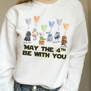 May include: White sweatshirt with Star Wars characters Darth Vader, BB8, Baby Yoda, R2D2, Stormtrooper, and Chewbacca, each with a Mickey Mouse balloon. The text "MAY THE 4TH BE WITH YOU" is printed in black.