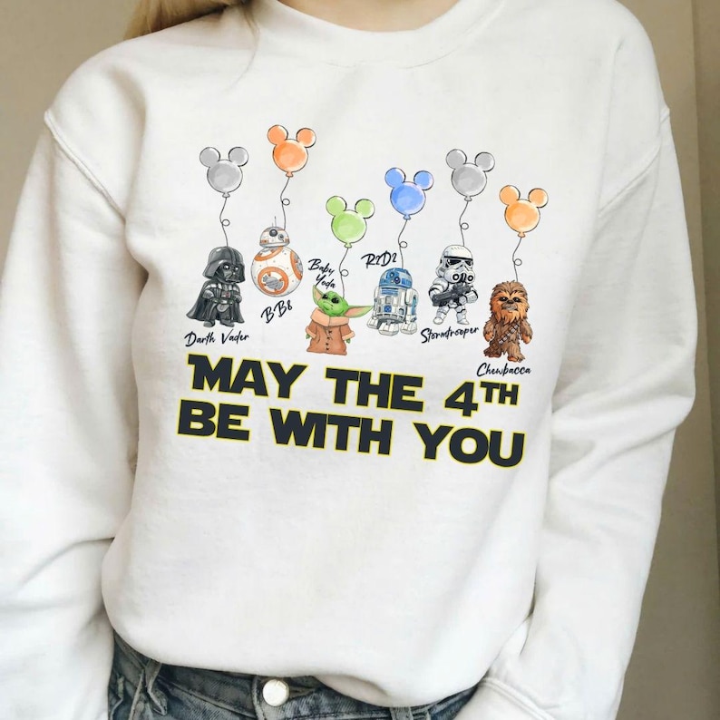May include: White sweatshirt with Star Wars characters Darth Vader, BB8, Baby Yoda, R2D2, Stormtrooper, and Chewbacca, each with a Mickey Mouse balloon. The text "MAY THE 4TH BE WITH YOU" is printed in black.