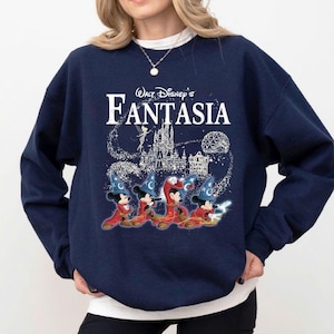 May include: Navy blue sweatshirt featuring the text "Walt Disney's Fantasia" in white. The design includes an illustration of Mickey Mouse in sorcerer attire, a castle, and a fairy. The sweatshirt is a comfortable, casual style.