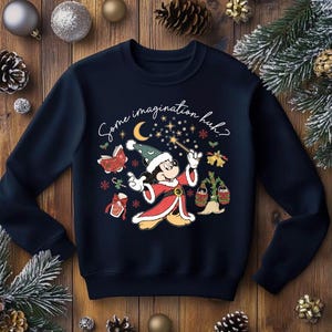 Könnte beinhalten: Marineblaues Sweatshirt mit Mickey Mouse als Zauberer, umgeben von weihnachtlichen Illustrationen. Der Text "Some imagination huh?" steht über der Figur. Festliches und skurriles Design.