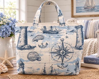 May include: A tote bag featuring a nautical print with blue and white illustrations of lighthouses, sailing ships, seashells, anchors, and a compass rose on a cream background. The bag has two fabric handles and a rectangular structure.