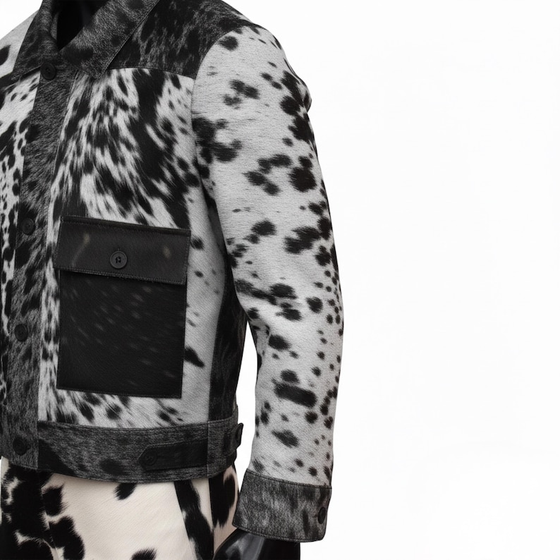 K&ouml;nnte beinhalten: Schwarz-wei&szlig;e Kuhfelljacke mit Knopfleiste, schwarzer Tasche und Kragen. Die Jacke hat ein gepunktetes Muster und ein klassisches Design.