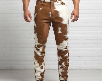 May include: Cowhide-patterned jeans with a brown and white spotted design. The jeans have a classic five-pocket design and a button and zipper closure. The model is wearing brown leather boots. The background is a white brick wall.