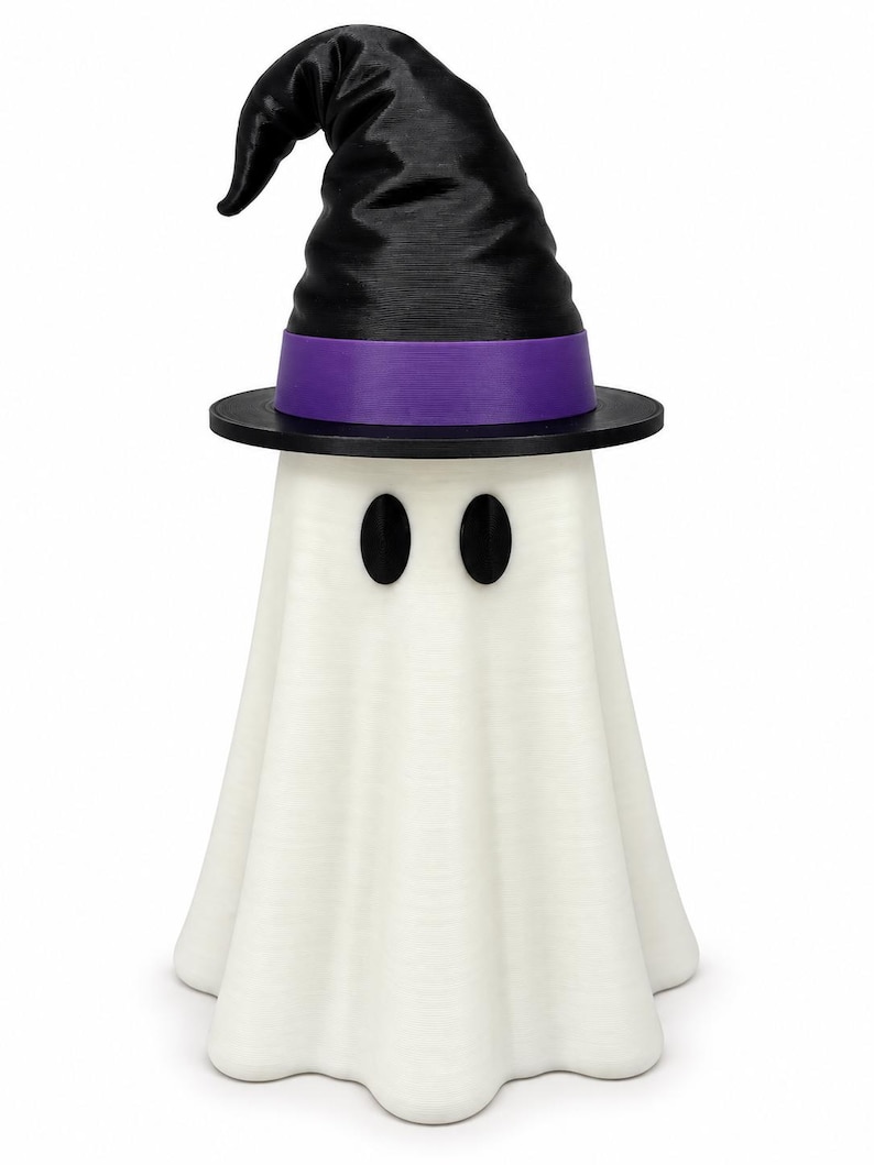 Puede incluir: Una figura de fantasma blanca con un cuerpo liso y drapeado y dos ojos ovalados negros. El fantasma lleva un sombrero de bruja negro puntiagudo con una banda morada ancha en la base. El objeto est&aacute; de pie sobre un fondo blanco liso.