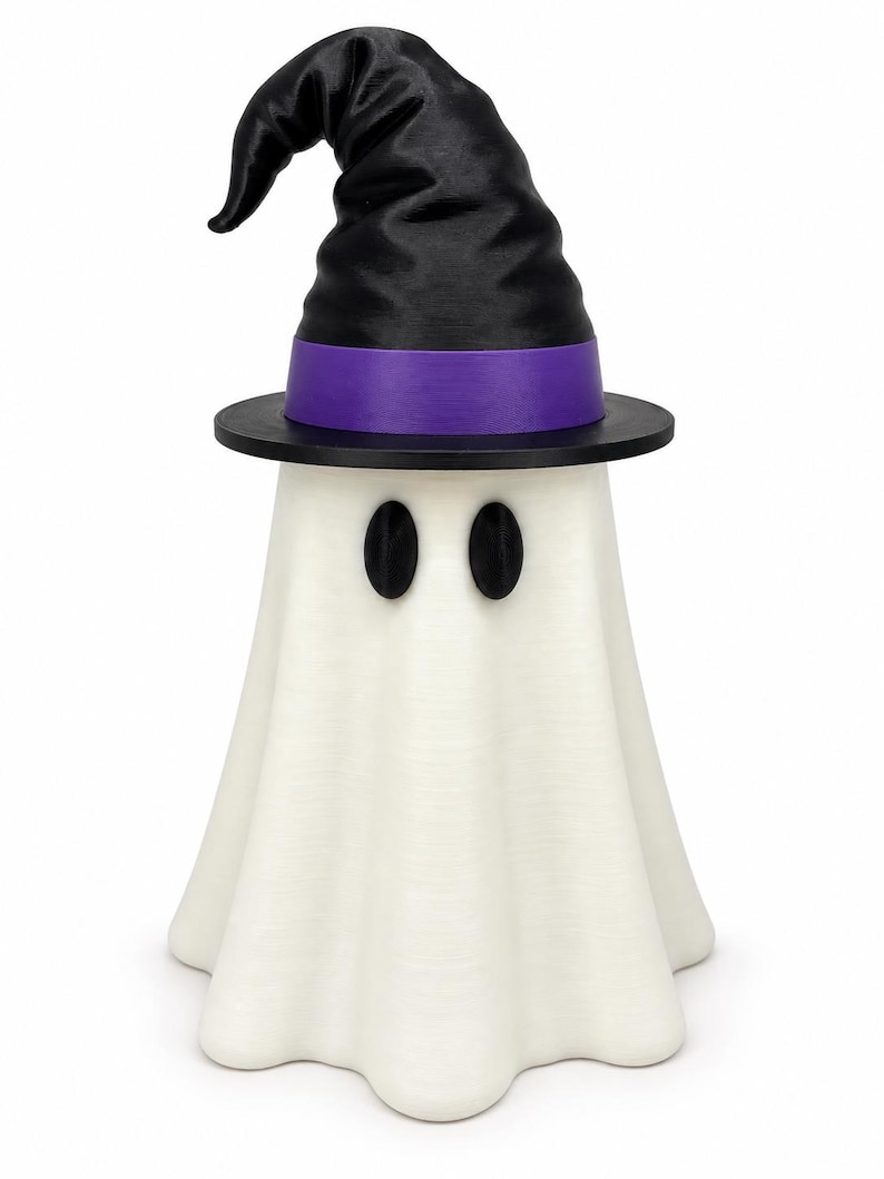 Puede incluir: Una figura de fantasma blanco que lleva un sombrero de bruja negro con una banda morada. El fantasma tiene dos ojos negros ovalados y un cuerpo drapeado y fluido. El sombrero presenta una parte superior puntiaguda y un ala ancha y negra.