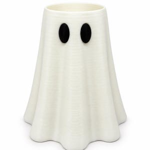 Puede incluir: Un recipiente cil&iacute;ndrico blanco y hueco con una base acampanada y crestas verticales, que recuerda a la forma de un fantasma. Presenta dos formas ovaladas negras prominentes orientadas verticalmente en la parte frontal superior.