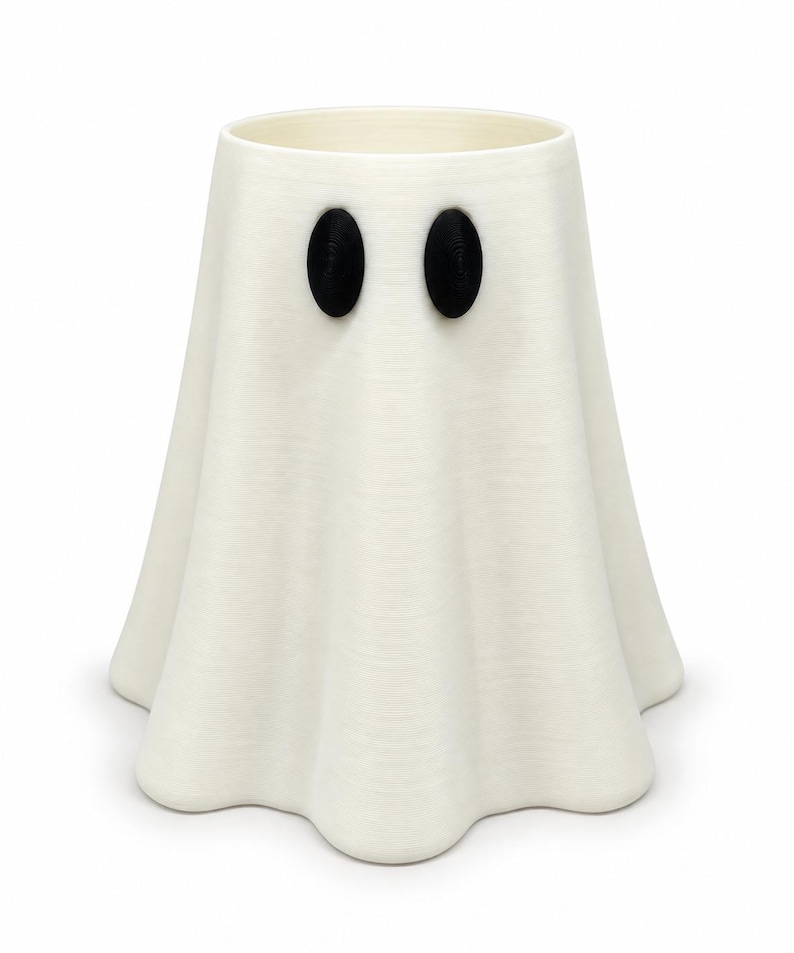 Puede incluir: Un recipiente cil&iacute;ndrico y hueco de color blanco con forma de fantasma y una base acampanada y ondulada. El objeto presenta dos ojos negros ovalados y prominentes, orientados verticalmente, situados cerca de la parte superior.