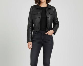 Op de afbeelding: Een zwarte leren jas met twee borstzakken en knoopsluitingen. De jas wordt gecombineerd met een zwarte skinny jeans en een zwarte top. De outfit is een klassiek, monochroom ensemble.