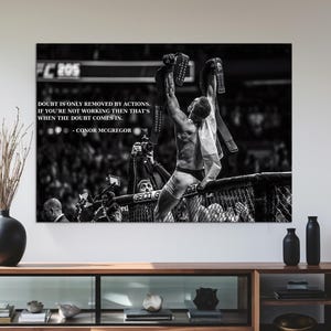 May include: Black and white framed print featuring a victorious athlete raising his arms. The print includes text: "Doubt is only removed by actions. If you're not working then that's when the doubt comes in." A modern, wooden media console is below.