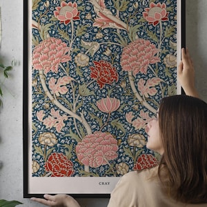 Puede incluir: Un póster enmarcado con un diseño floral en tonos rosa, rojo y verde sobre un fondo azul oscuro. El póster tiene el texto "WILLIAM MORRIS CLASSIC TEXTILE PATTERN DESIGN" en la parte superior. La palabra "CRAY" está en la parte inferior.