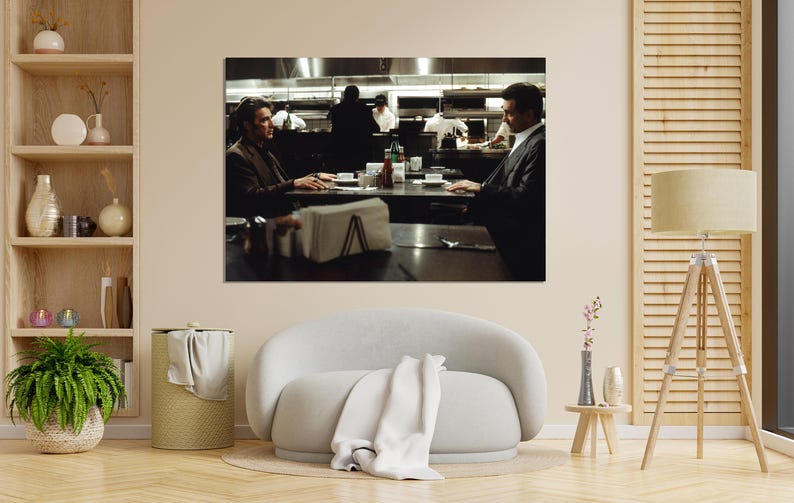 May include: A framed print of a scene from a film, featuring two men seated at a table in a restaurant. The image has a dark, cinematic aesthetic, with a focus on the characters and their interaction. The background shows a kitchen.