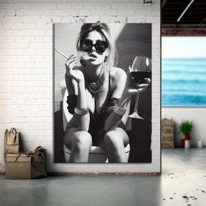 May include: Black and white portrait of a woman wearing sunglasses, jewellery, and holding a cigarette and a glass of red wine. The woman is seated on a toilet. The image is a portrait.