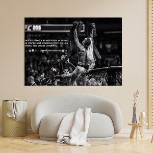 May include: Black and white photograph of a victorious athlete in a fighting ring, holding up championship belts. The image includes text that reads "Doubt is only removed by actions. If you're not working then that's when the doubt comes in."