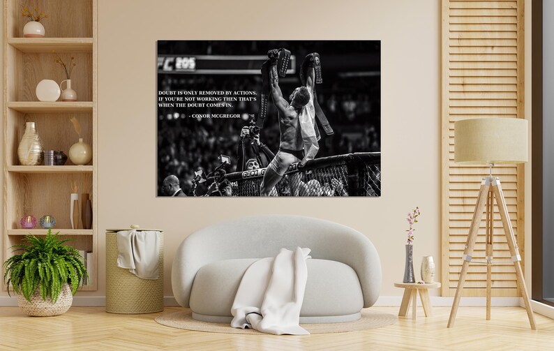 May include: Black and white photograph of a victorious athlete in a fighting ring, holding up championship belts. The image includes text that reads "Doubt is only removed by actions. If you're not working then that's when the doubt comes in."