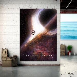 Op de afbeelding: Een groot poster met een kosmische scène met een zwart gat en helder licht. De poster heeft het woord "INTERSTELLAR" onderaan en een citaat over vooruitgang. De poster hangt aan een witte bakstenen muur.
